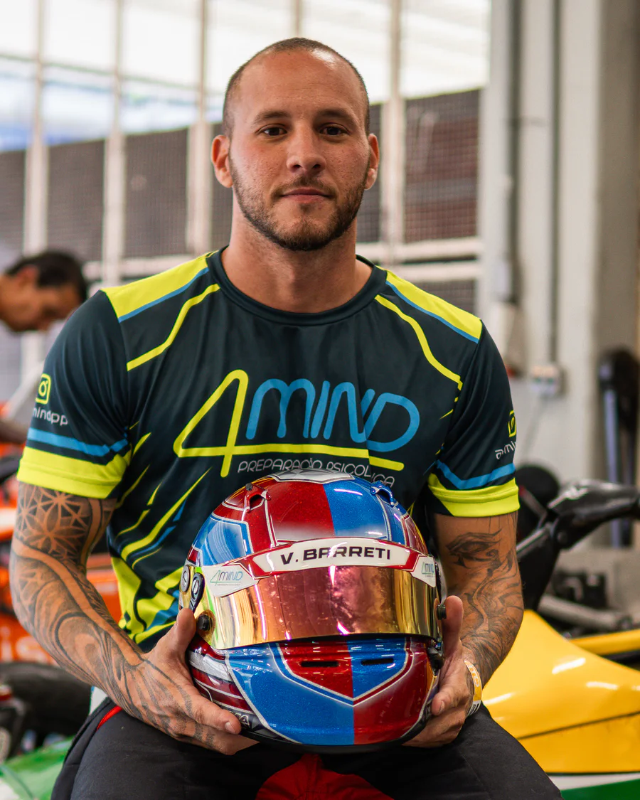 Vinícius Barreti no paddock, segurando um capacete diante de carros de Fórmula Vee.